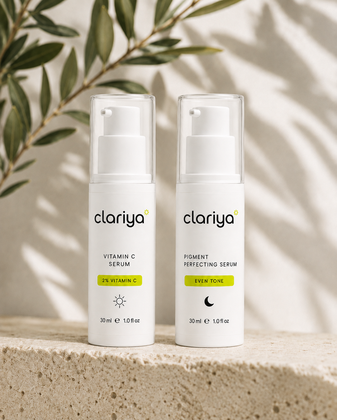 The CLARIYA Vitamin C Serum and Pigment Perfecting Serum standing side by side on a travertine ledge with an olive branch and soft daylight shadows.